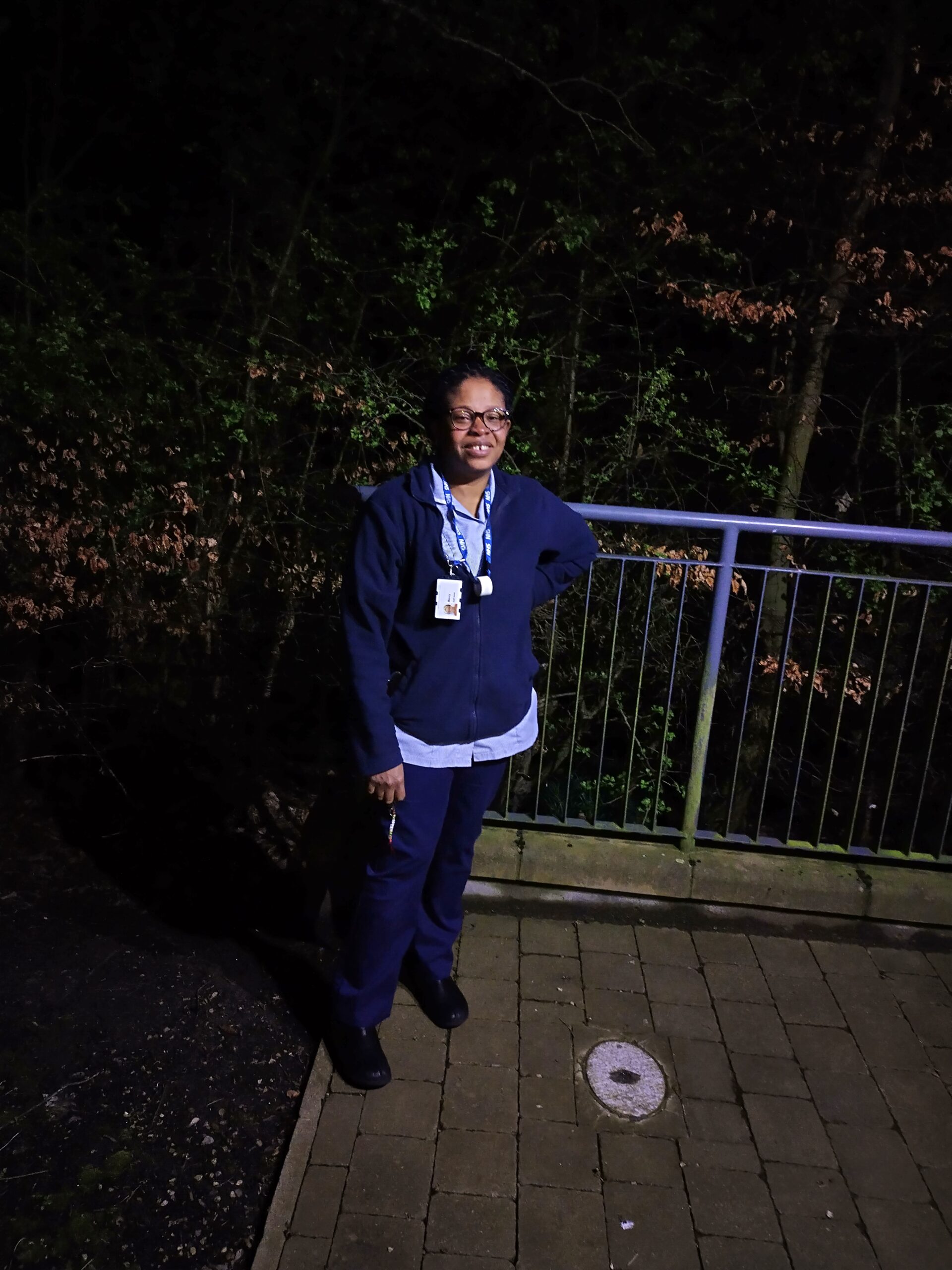 A nurse standing in on a patio with trees behind her at night.