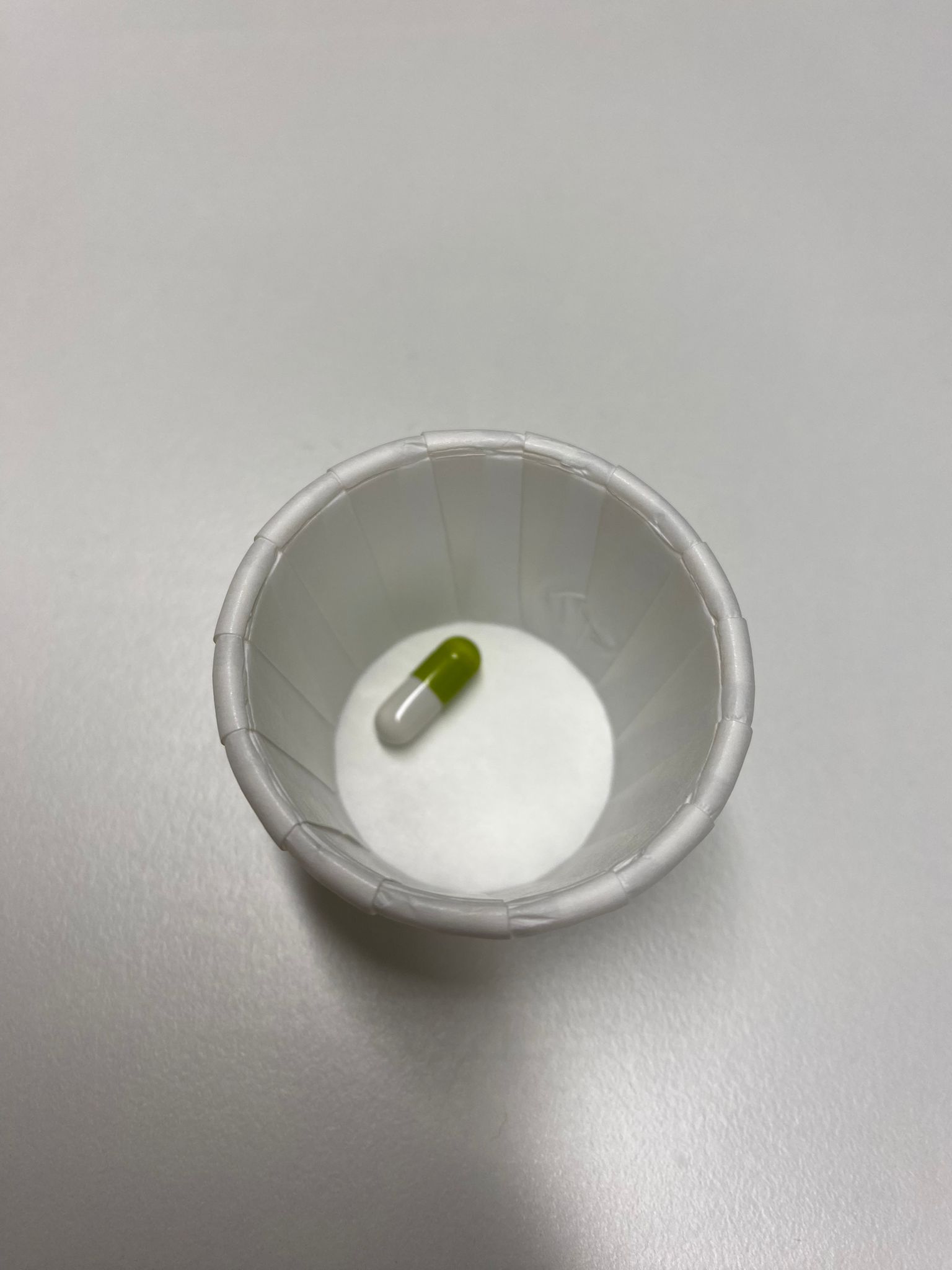 A white paper bowl with a green and white pill in it.
