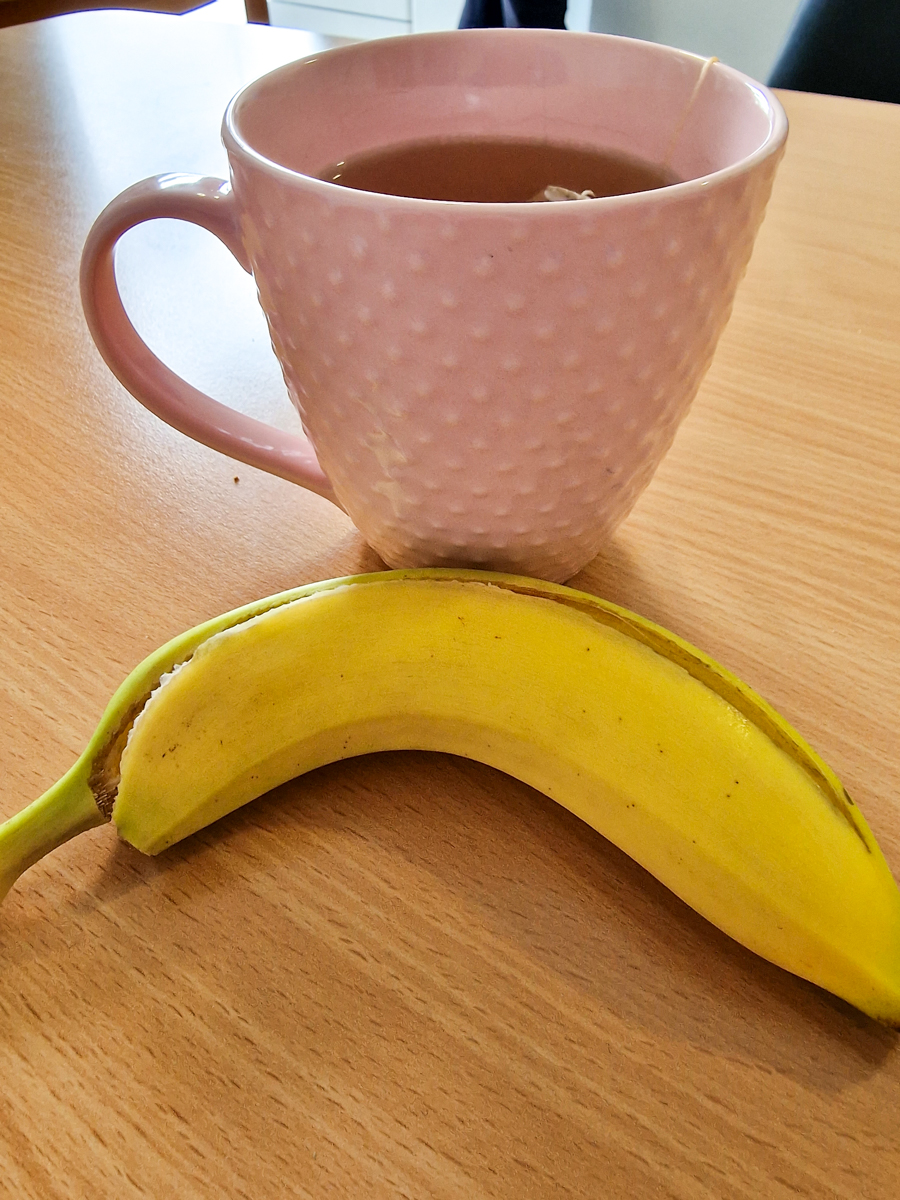 A banana on a table next to a cup of tea.