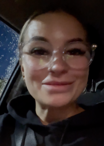 A woman in glasses is taking a selfie in a car.