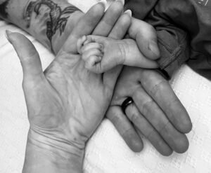 A black and white photo of a woman holding a baby's hand.