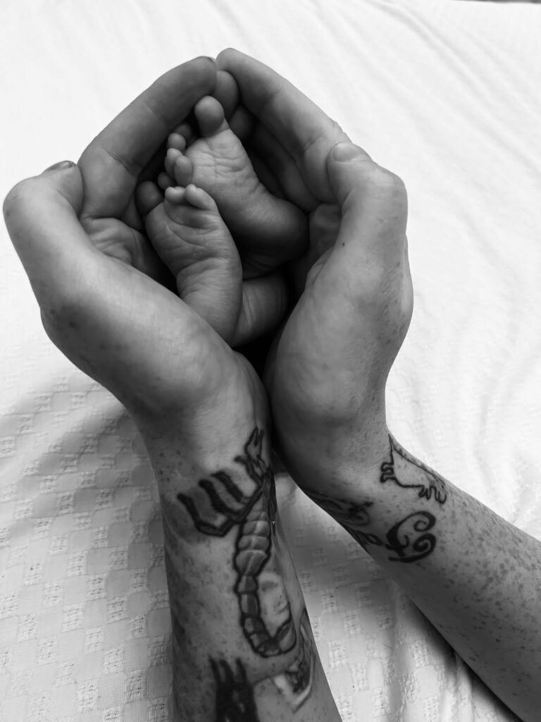 A black and white image of a pair of hands gently holding a newborn baby.